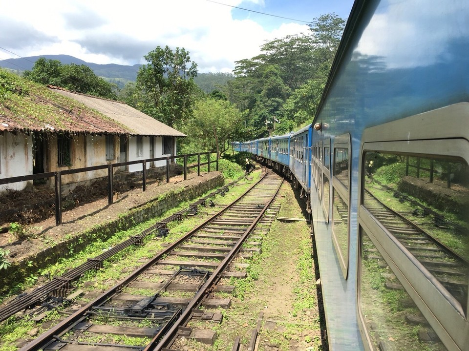 Sri Lanka - Kandy - An der nächsten Station steigt dann doch jemand dazu und ich muss den Fensterplatz freigeben. Die Dame ist Lifecoach aus Beirut und teilt mit mir ihr Frühstück. Top!
Die erste Klasse ist klimatisiert und mit mehreren Fernsehern ausgestattet - es läuft ein Stallone Actionfilm. Da der Bahnhof in Kandy ein Kopfbahnhof ist, fahren wir mit dem Rücken in Fahrtrichtung los. Soweit erstmal alles gut, bis ein Einheimischer seinen Sitz dreht. Ach das geht? Auf einmal bricht im Abteil Chaos aus. Ich war in der letzten Reihe und hinter meinem Sitz war Platz für meine Tasche. Nachdem ich den Sitz gedreht habe, brauche ich den Platz für die Füße. Die Tasche kann aber nicht mehr hinter den Sitz, da dort schon der nächste Gast sitzt. Das Problem haben nun noch mehr Leute und es braucht ca 30 min bis sich alle gedreht und einen Platz für das Gepäck gefunden haben. Herrlich. Eine schöne Kettenreaktion.