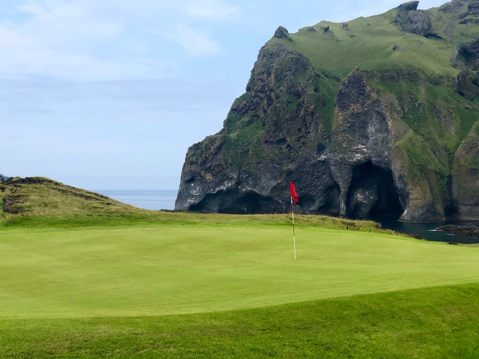 Island - Vestmannaeyjar - Ah! Ich glaube, da hinten sehe ich ihn schon… Normal kann man den Stein bei einer Bootsfahrt rund um die Insel bewundern, dafür haben wir aber keine Zeit. Von daher heisst es für uns quer über den Golfplatz zu traben. Darf man das?