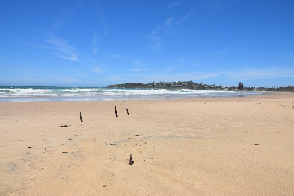 Australien - Yamba - Die vier unscheinbaren Holzspitzen gehören zum Schiffswrack "The Buster", das hier 1893 am Strand auflief