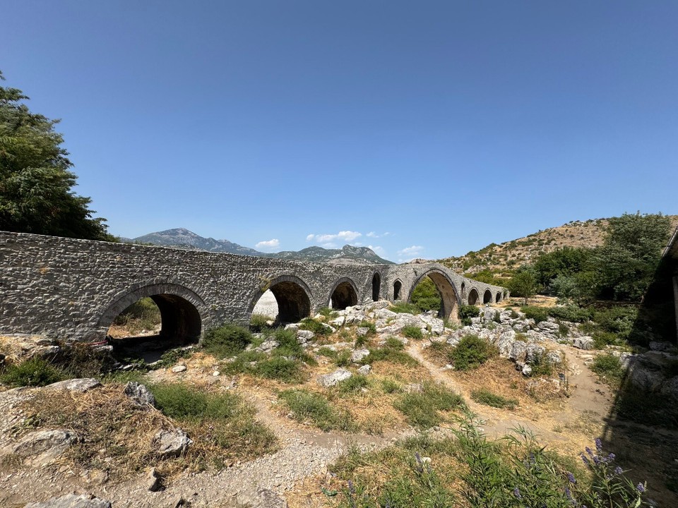 Albanien - Shkodër - Die Ura e Mesit ist eine ottomanische Bogenbrücke in Nordalbanien rund acht Kilometer östlich von Shkodra. Die vermutlich im 18. Jahrhundert erbaute Brücke passt sich schön in die Landschaft ein, nur fließt um diese Jahreszeit kaum Wasser.